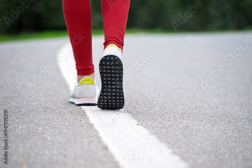 Close up of a woman runner walking along a road wearing white sneakers and red leggings