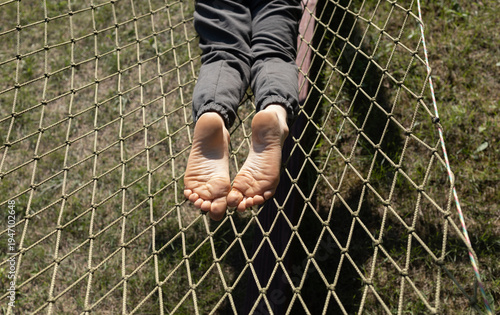 child's bare feet, lying and relaxing in a hammock outdoors on a sunny summer day. Concept of tourism, active lifestyle, interesting, carefree childhood. Lazy weekend
