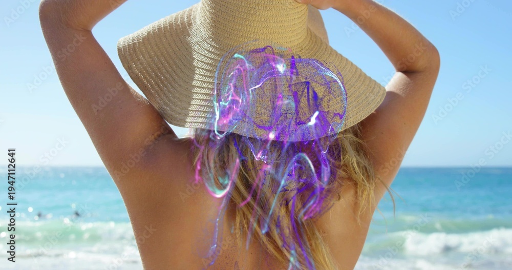 Obraz premium Standing woman holding wide-brim straw sunhat at sandy shore, showing swimsuit and purple hologram