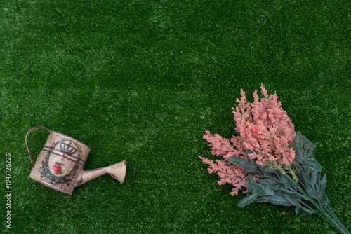 Vintage watering can and pink flowers on green grass background with copy space.