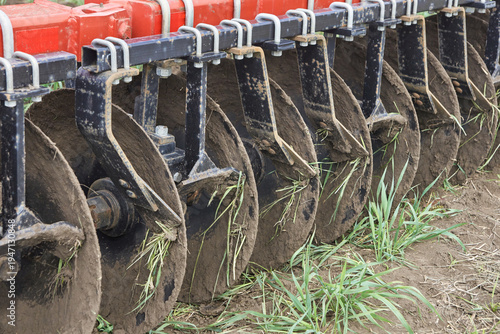 Obraz na plátne Close up of agricultural disc harrow blades cutting soil with grass in field during cultivation process