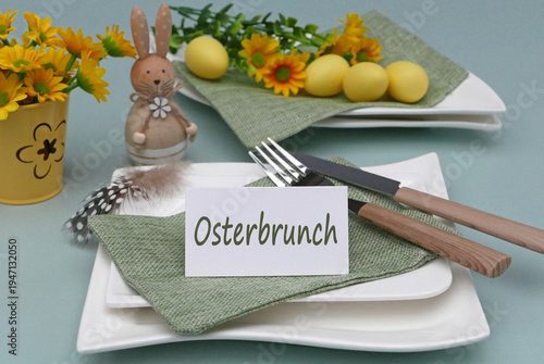 Teller mit Osterdekoration bestehend aus einem Osterhasen bemalten Eiern, Besteck auf grüner Stoffserviette und einem Schild mit der Aufschrift Osterbrunch.