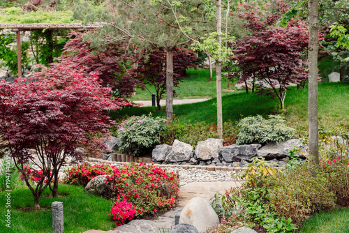 Tableau sur toile Spring Japanese garden with red maple trees, flowers and stone path in peaceful