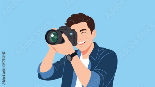 Smiling young male photographer holding a professional DSLR camera and taking a creative picture against a solid blue background.
