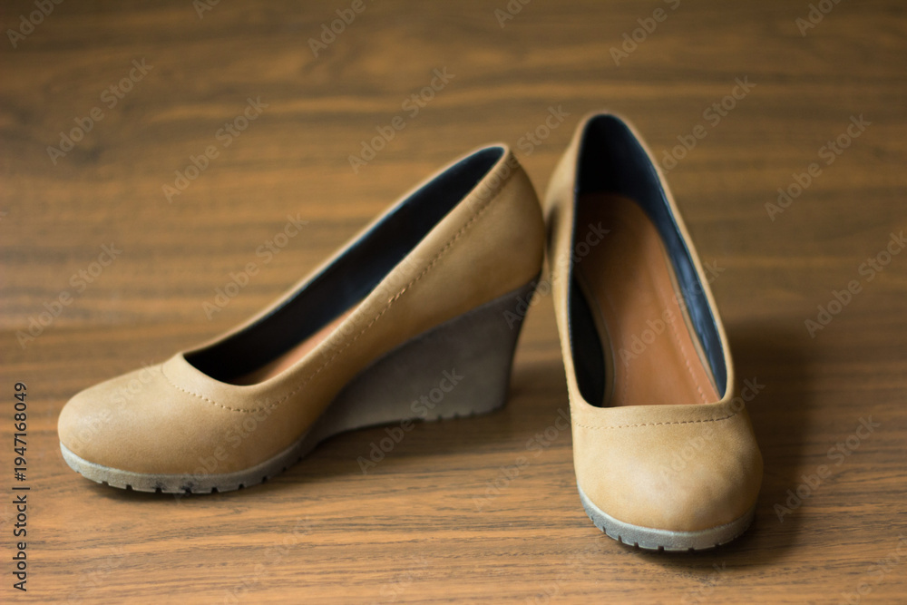Naklejka premium Pair of tan suede women's wedge heel shoes on a brown wooden background