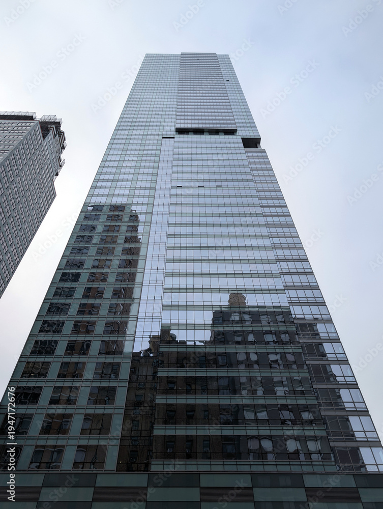 Naklejka premium Reflective glass skyscraper towering above older New York buildings, capturing the blend of modern and traditional architecture in the city, travel USA