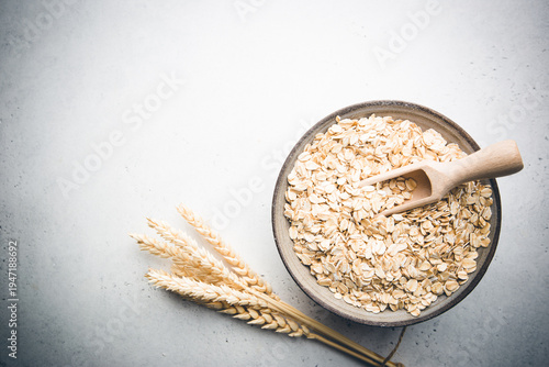 Rolled oats or oat flakes in bowl and wooden spoon on white table, top view with copy space