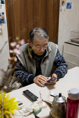 Senior mature middle aged man holding cell mobile phone using smartphone sitting at home on a chair, scrolling social media, checking financial apps, buying online, texting messages.