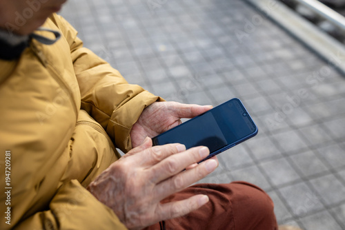 An close-up of an older man sitting on a bench  looking at his mobile phone