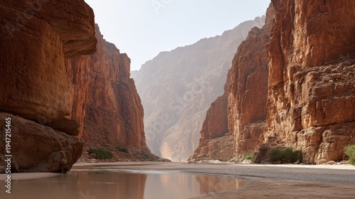 Towering reddish rock formations flank a shallow river cutting through a dry canyon landscape