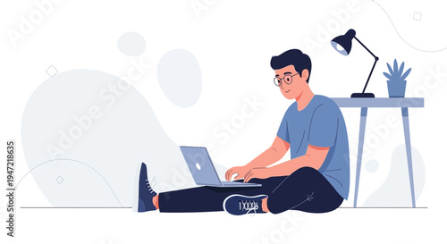 Young man working on laptop on floor, desk with lamp and plant in background