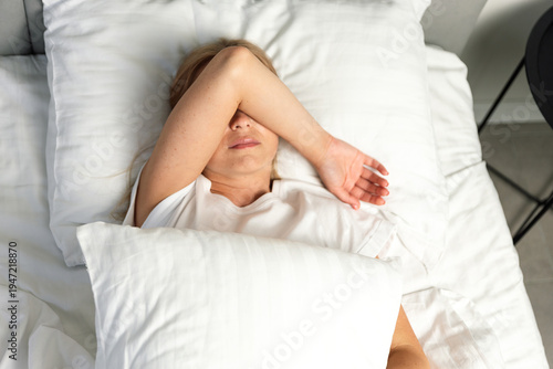 Obraz na płótnie Young woman lying in bed covering eyes with arm in bright bedroom