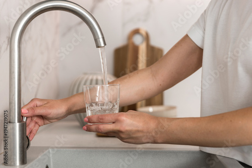 Woman fills a glass with water from the kitchen faucet in a clean home