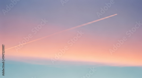 A thin airplane contrail streaks diagonally across a vast sky gradient transitioning from soft pink and peach tones to pale blue.