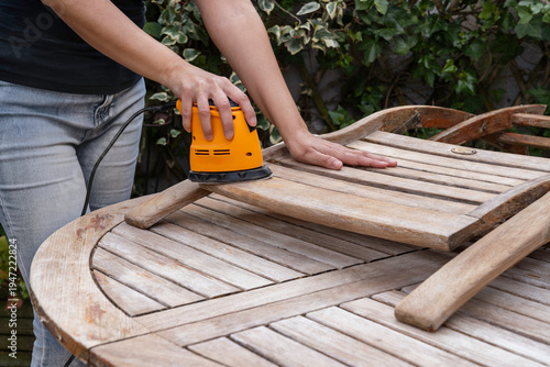 
An unrecognizable person with a homemade sander prepares their garden furniture for the arrival of warmer weather.
A woman with a sander on her small terrace