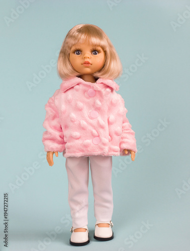 A full-length doll toy with beautiful blond hair and a cute face in stylish clothes on a blue background. These are stylish dolls for modern children.