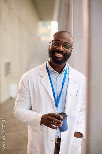 Happy black doctor with cup of coffee at medical clinic looking at camera.