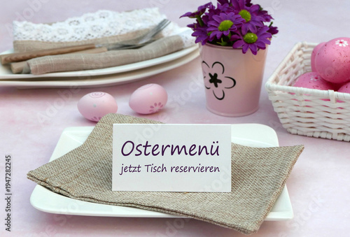 Tischdekoration zu Ostern mit Osterhasen, Ostereiern, Besteck auf Stoffserviette und einem Schild mit der Aufschrift Ostermenü jetzt Tisch reservieren.