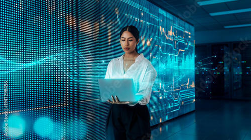 Data analyst working on laptop with digital market charts, Latin woman