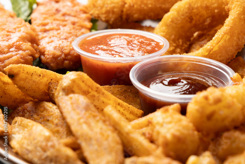 Close up appetizer sampler with chicken tenders onion rings potato wedges and dipping sauces