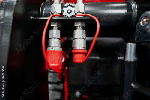 Close up of red capped hydraulic quick couplers mounted on black industrial machinery, showing metal fittings and pressure line connections indoors