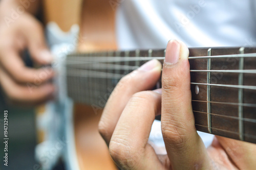 Close-up of a musician's hand pressing strings on an electric guitar fretboard. Concept of musical performance, learning guitar, and creative hobby.