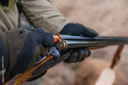Hunter hands in tactical gloves reloading a double barreled shotgun with a shotgun shell, preparing for hunting