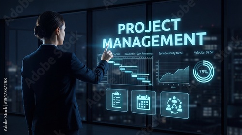 A business professional interacts with a digital display showing project management data. The office has a view of city lights at night. The person points at charts and graphs