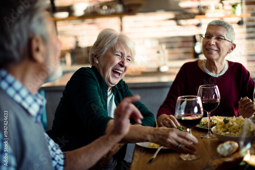 Senior friends laughing over dinner in cozy kitchen
