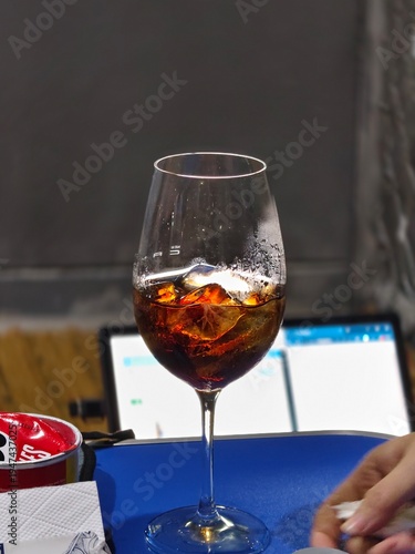 Refreshing iced soft drink in a wine glass on a table with laptop background.