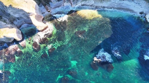 Scenic aerial view of a rugged coastal landscape featuring sea waves, rocky cliffs, clear blue water and untouched nature.