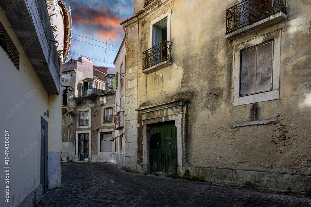 Obraz premium A narrow cobblestone alley with abandoned residential buildings in the medieval hillside Alfama district of Lisbon, Portugal.