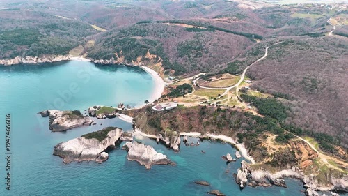 Scenic aerial view of a rugged coastal landscape featuring sea waves, rocky cliffs, clear blue water and untouched nature.