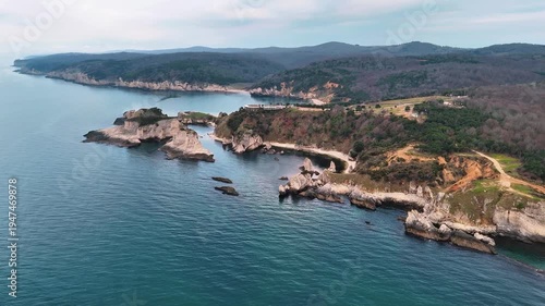 Scenic aerial view of a rugged coastal landscape featuring sea waves, rocky cliffs, clear blue water and untouched nature.
