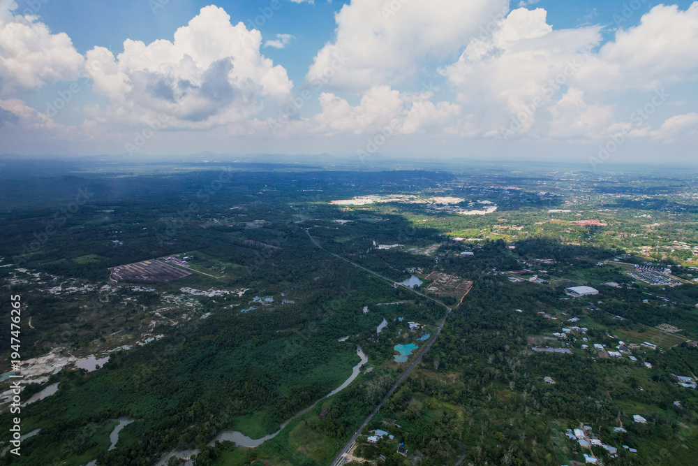 Obraz premium Aerial landscape of a rural area in Belitung, Indonesia. The wide drone shot captures a mix of palm oil plantations, kaolin mines, winding rivers, and green forests under a cloudy sky.