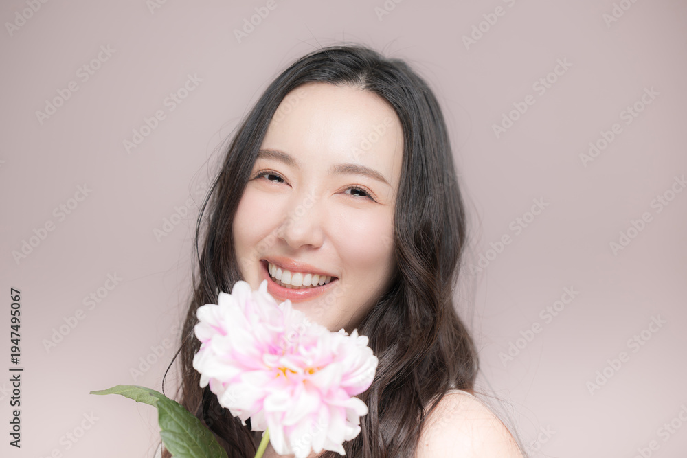 Fototapeta premium ダリアの花を持って多幸感にあふれるピンクの春色イメージの女性の美容ビューティーイメージカメラ目線 ピンク背景