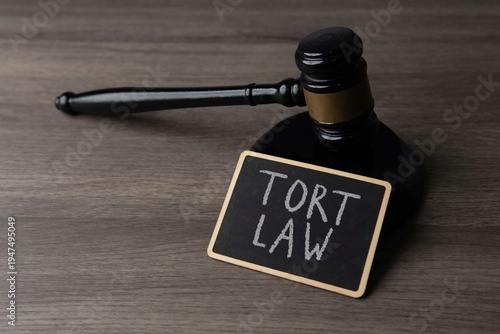 A judge's gavel and a chalkboard with text TORT LAW on a wooden desk. Civil litigation, personal injury claims, legal liability, and judicial proceedings concept.