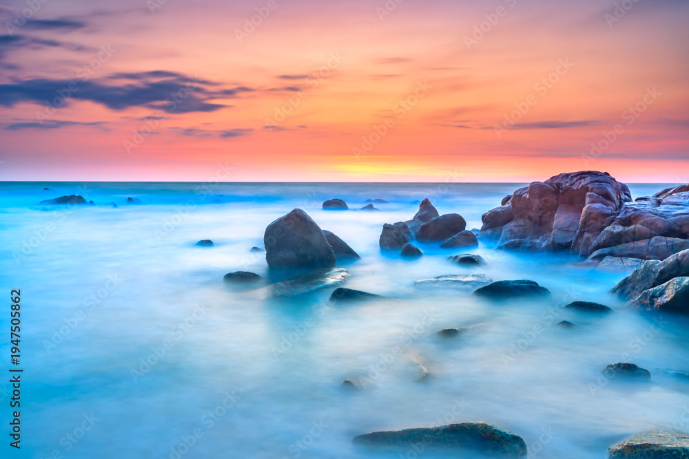 Obraz premium Beautiful coastal sunrise scene featuring a dramatic rock formation rising from a sandy beach.