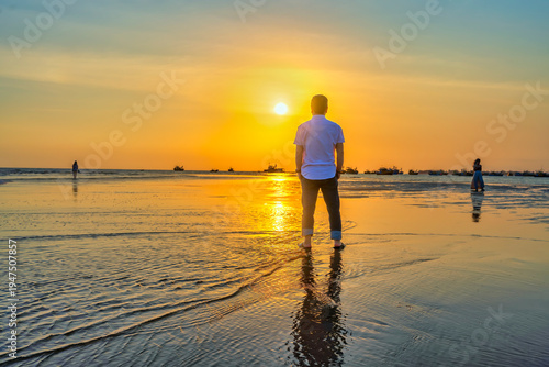 Wallpaper Mural The silhouette of a man stands alone on a wide sandy beach while watching a vibrant sunset over the ocean. Torontodigital.ca