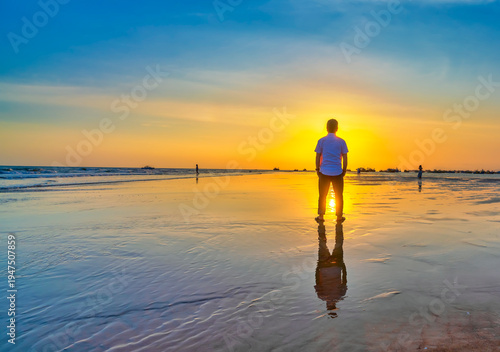 Wallpaper Mural The silhouette of a man stands alone on a wide sandy beach while watching a vibrant sunset over the ocean. Torontodigital.ca