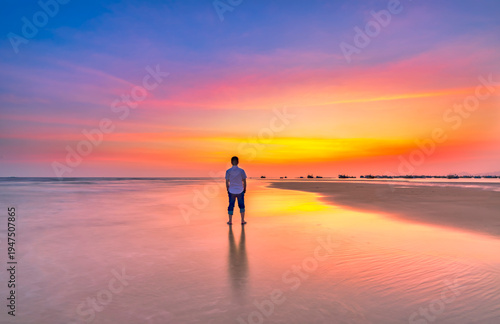 Wallpaper Mural The silhouette of a man stands alone on a wide sandy beach while watching a vibrant sunset over the ocean. Torontodigital.ca