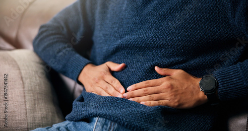 Photos Man, hands or stomach ache with pain for indigestion, constipation or diarrhea on sofa in home