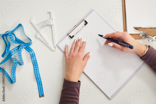 Nutritionist doctor writing diet plan on table with measuring tape, view from above