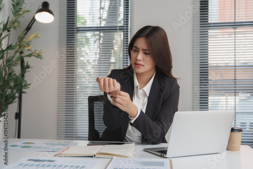 Schilderij op canvas Asian businesswoman feeling wrist pain working at desk