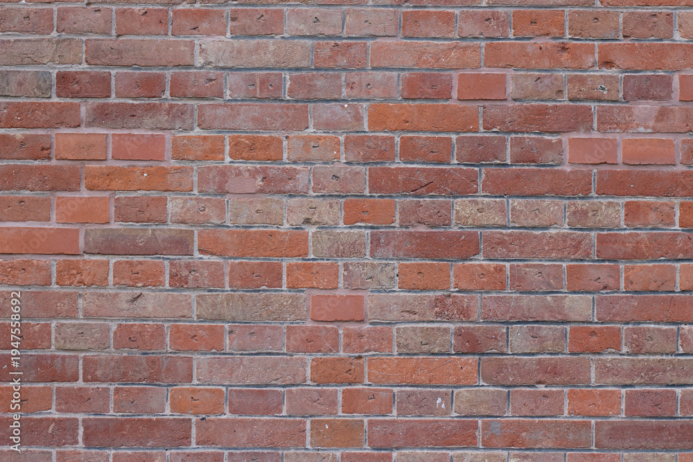 Obraz premium Textured red brick wall with varying shades and sizes of bricks, showcasing a rustic and aged appearance suitable for architectural backgrounds or design projects
