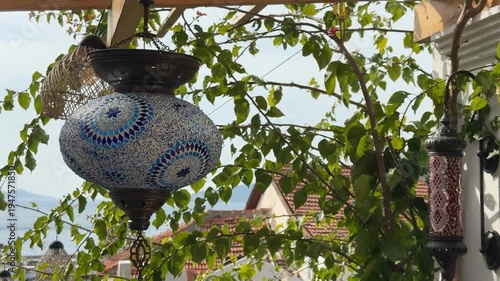 Mosaic lantern hanging among green leaves on a sunny day, background