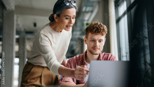 Seasoned female creative director providing supportive hands-on feedback to a focused junior designer during a digital project review.