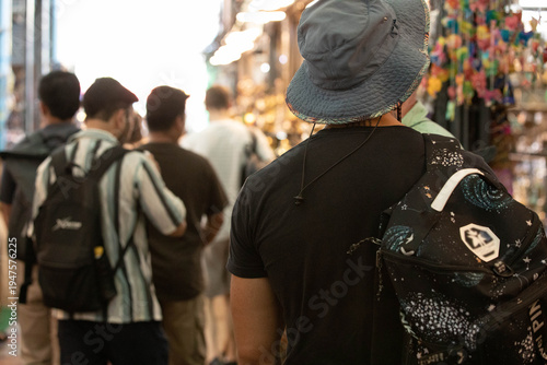 Man backpack walking in outdoor market area, local vendor street commerce, Thai weekend market lifestyle, rear view, at Chatuchak Market.