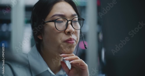 Asian Female Trader Receives Call Via Headset While Monitoring Financial Data in Modern Stock Exchange Office. Woman Listens Bad News About Market Performance, Expression Shifts Concern and Distress.