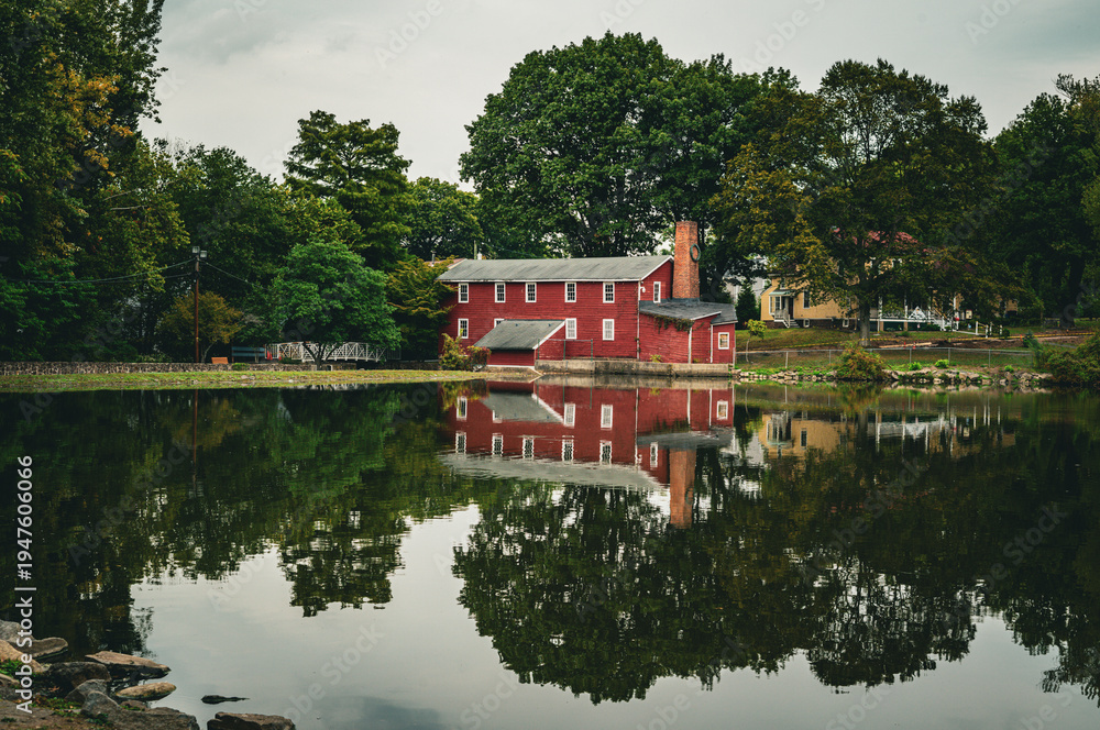 Obraz premium Red barn surrounded by trees reflecting on a calm lake in autumn countryside